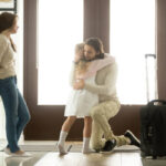 Sad father hugging little daughter before leaving for long business trip, upset dad embracing crying girl saying goodbye to daddy at home in hall with baggage, family separation, good bye, farewell