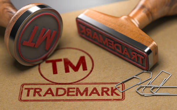 3D illustration of two rubber stamps with the word trademark and the symbol TM over brown paper background. Trade-mark Registration Concept